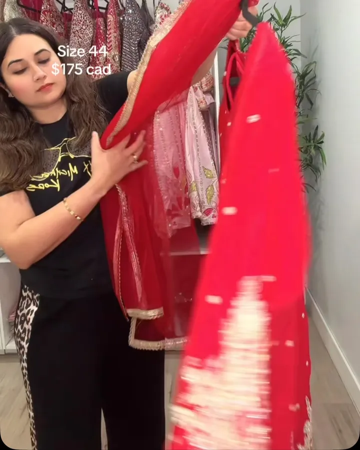 Rose red suit and sheer dupatta held up by a team member in the boutique